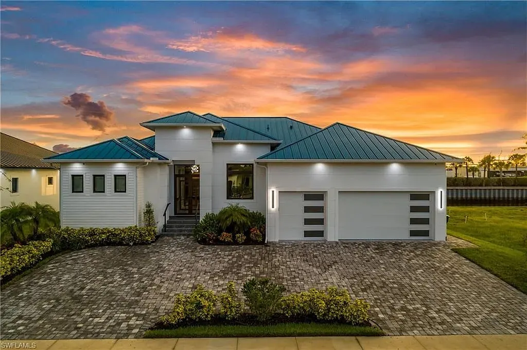 Front of the Bluewater Residence at dusk, a white single-story home with a blue standing-seam metal roof, a two-car garage and a paver driveway.
