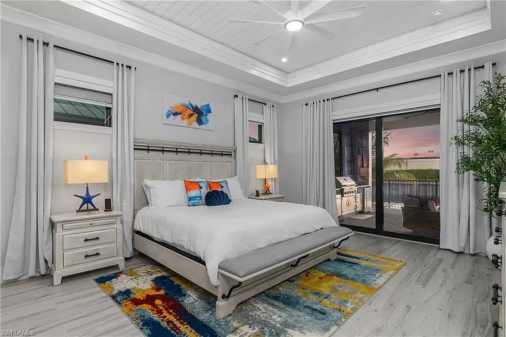 Bedroom with a planked tray ceiling, a white bed and sliding glass doors to the covered lanai and outdoor kitchen.