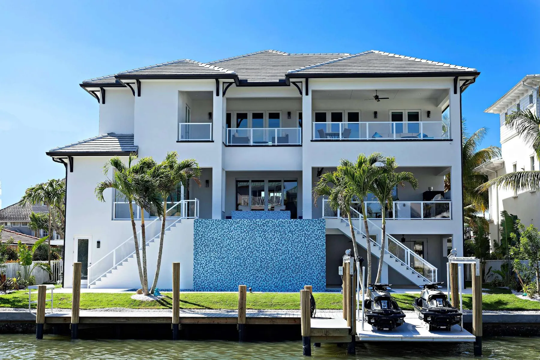Rear elevation facing the canal with a glass-tile feature wall, stairs and a private dock.