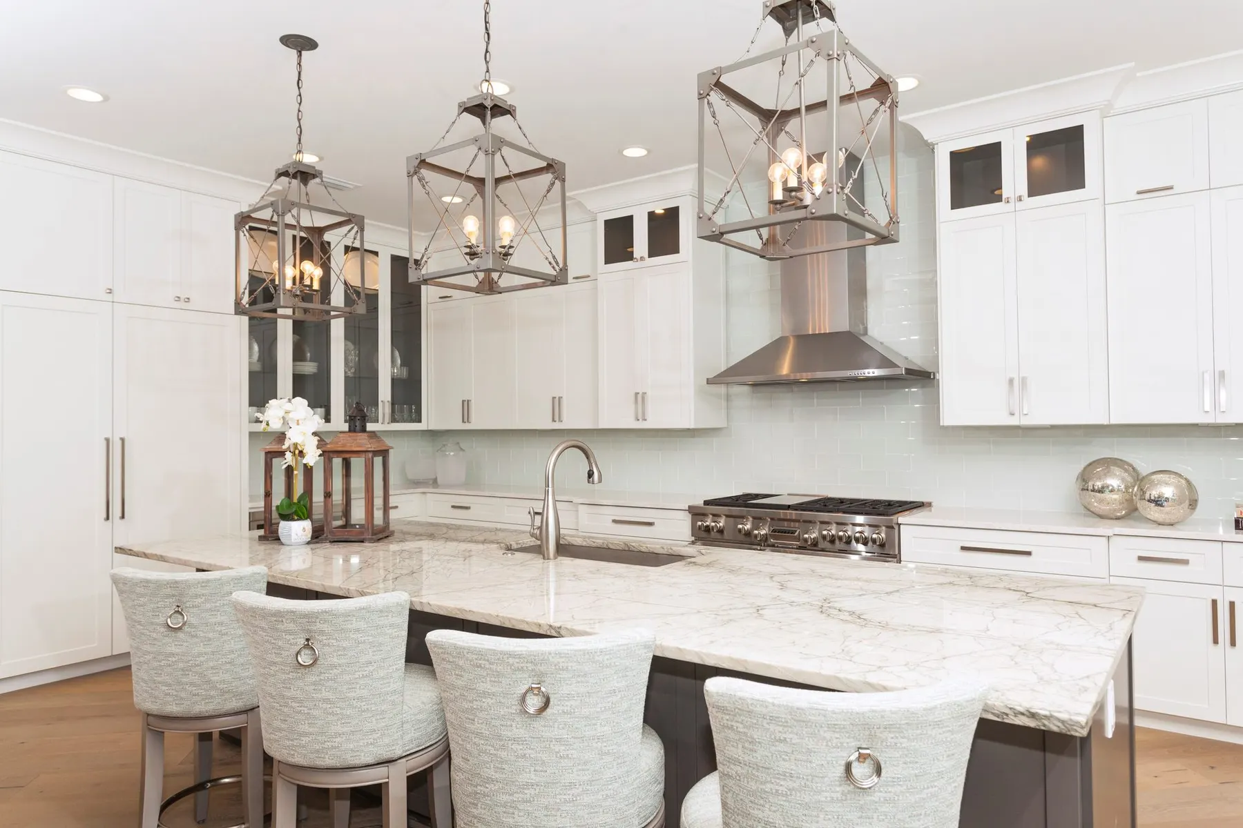 White kitchen with a large island, lantern pendants and a stainless range hood.