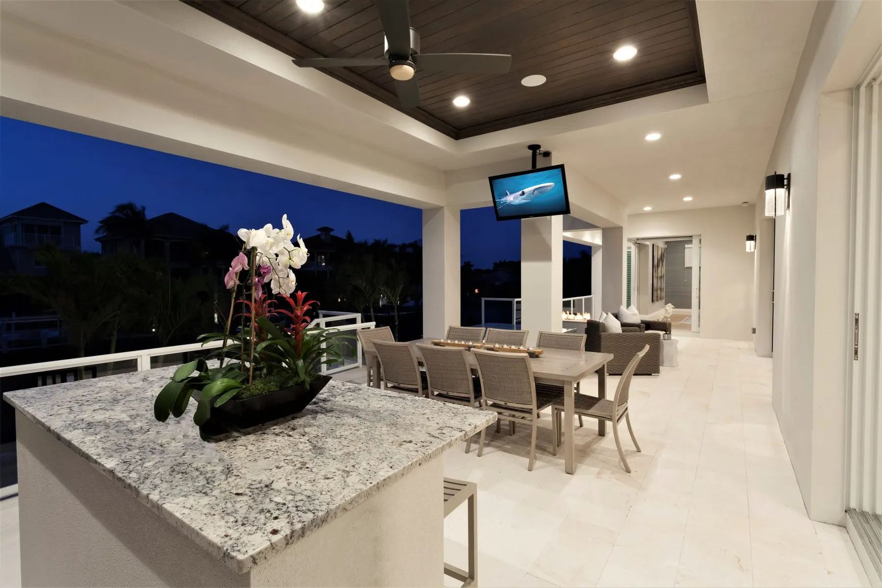 Covered outdoor kitchen and dining area with a wood-lined ceiling at dusk.