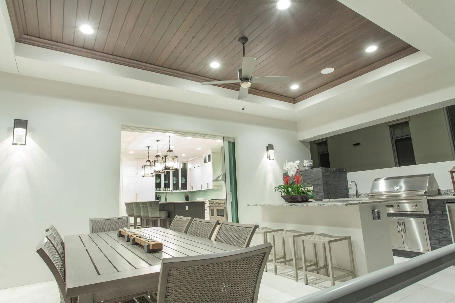 Outdoor dining and kitchen under a wood-planked tray ceiling.