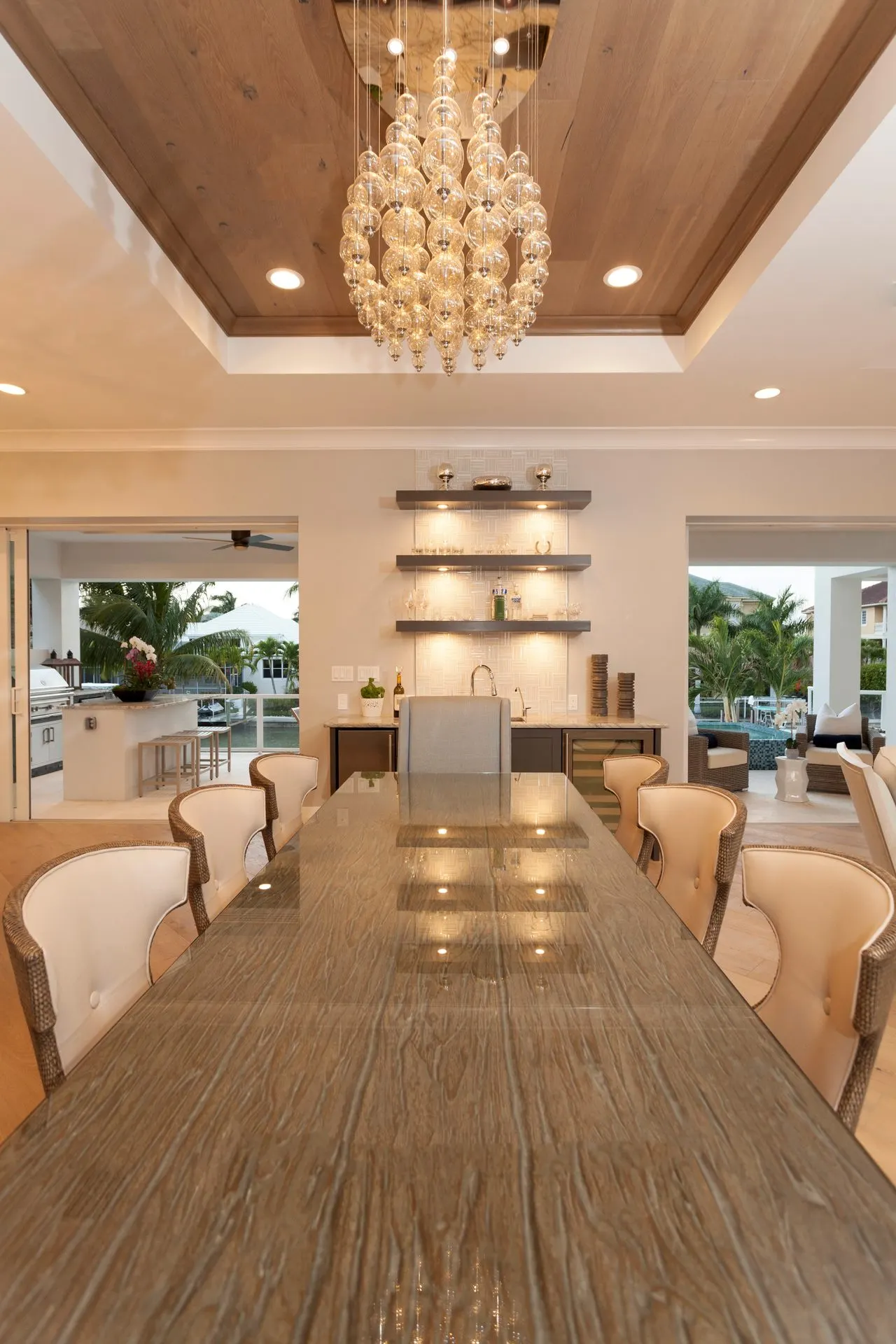 Long dining table beneath a shell chandelier and wood ceiling.