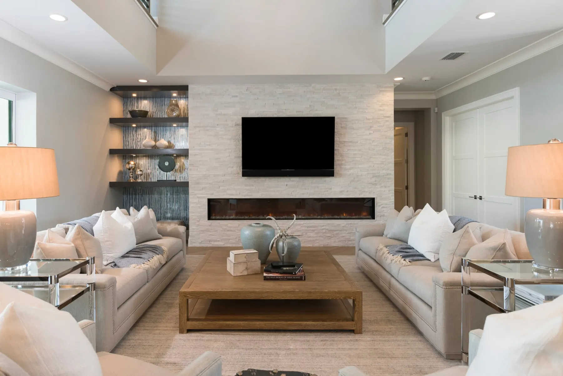 Living room with a linear fireplace, stone feature wall and lit display shelving.