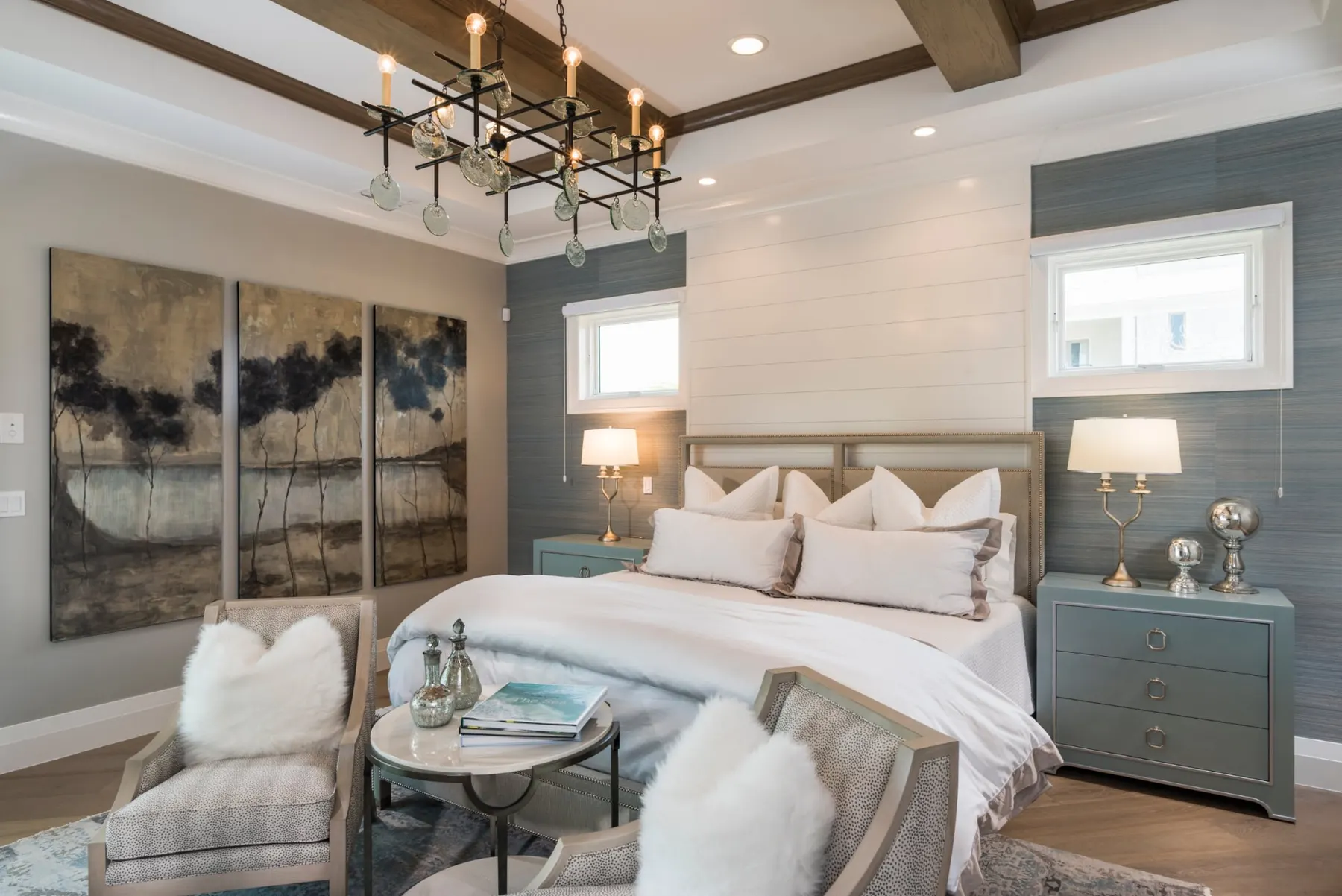 Bedroom with a beamed tray ceiling, iron chandelier and an upholstered bed.