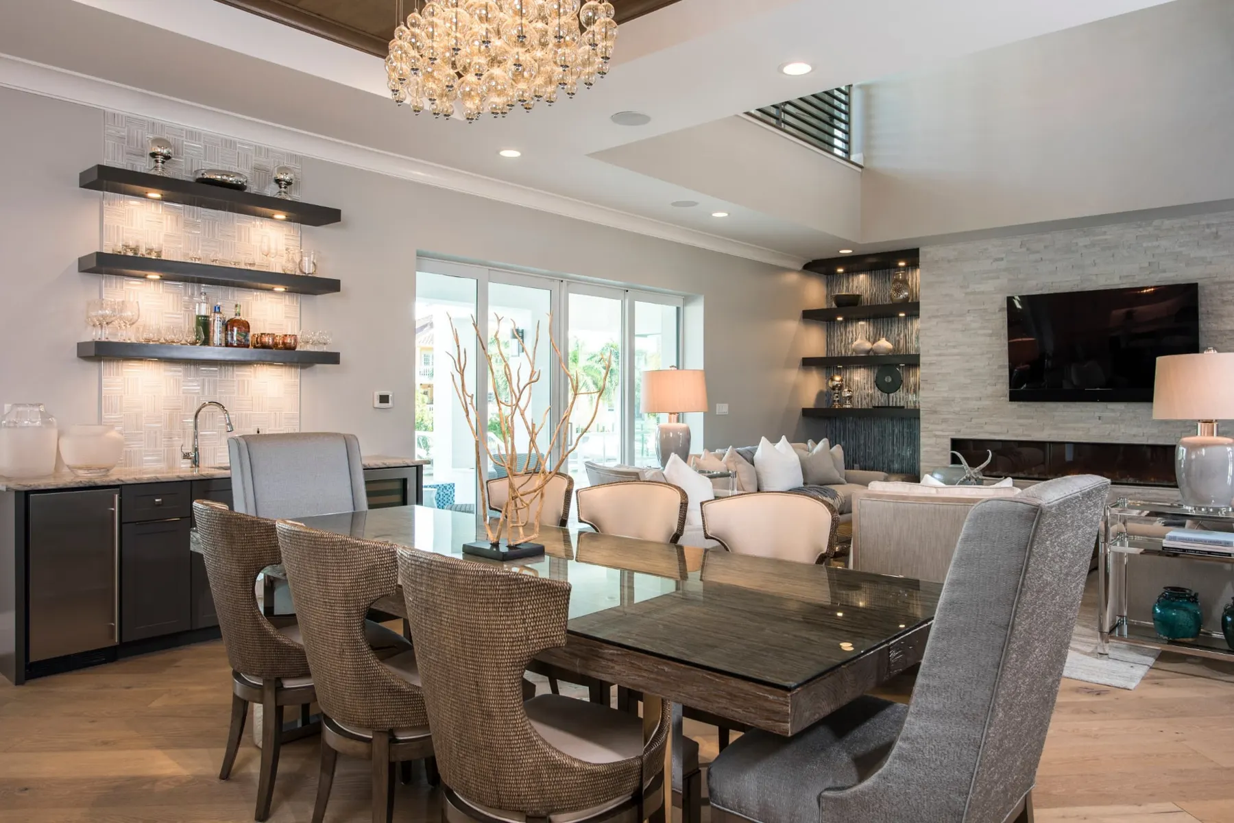 Dining table beside the living area with floating shelves and a wet bar.