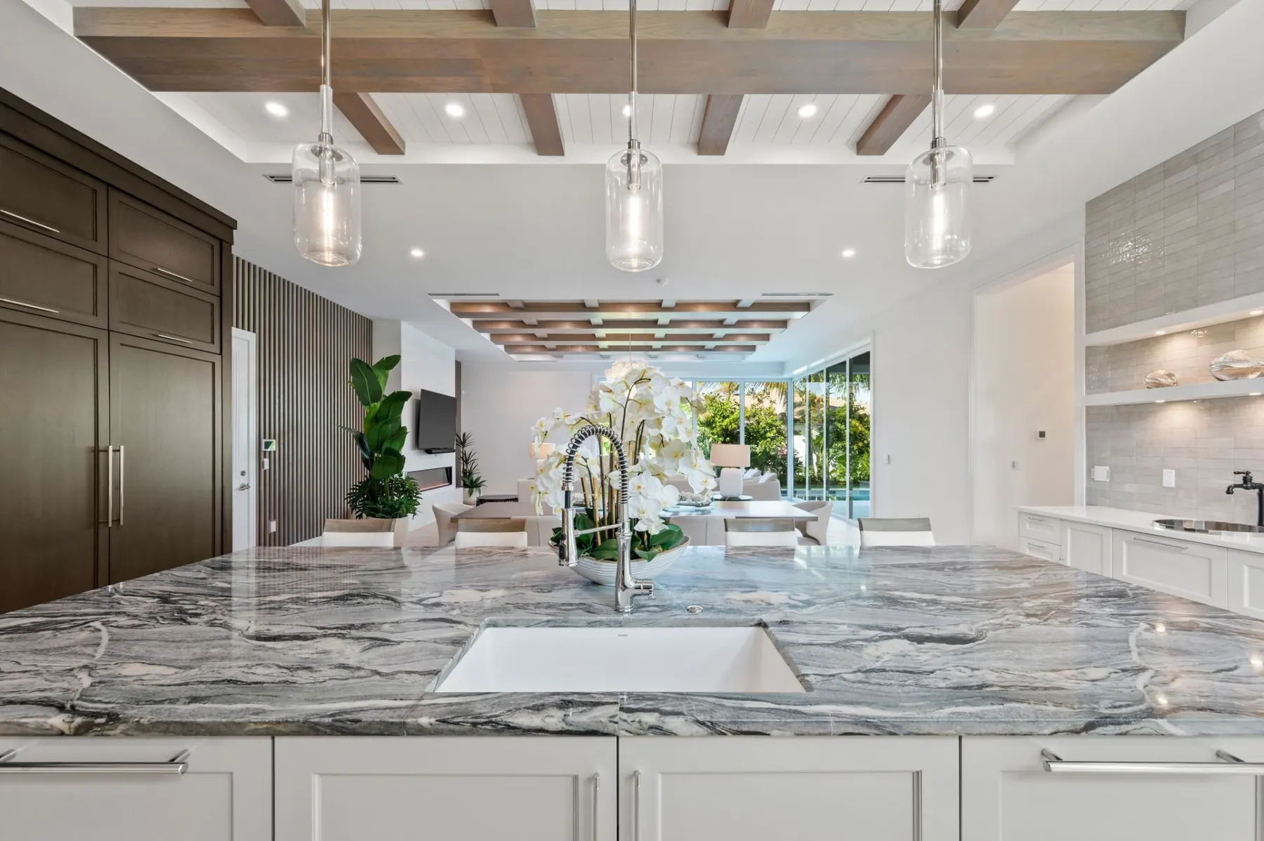 Kitchen island with a stone top, an undermount sink and glass pendants under a beamed ceiling.