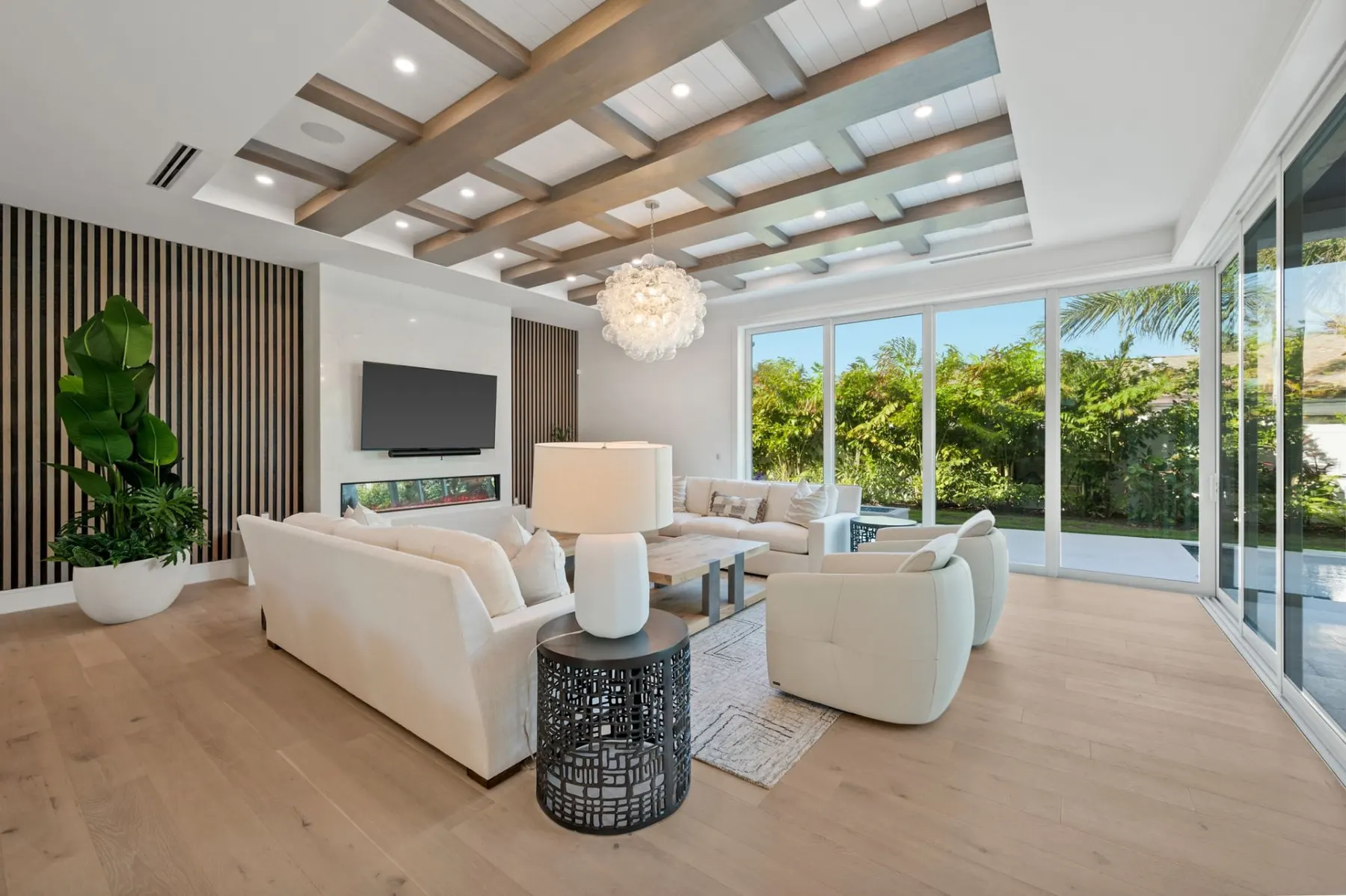 Living room with a slatted wood feature wall, a wall-mounted television, a linear fireplace and a bubble chandelier, with glass doors to the pool.