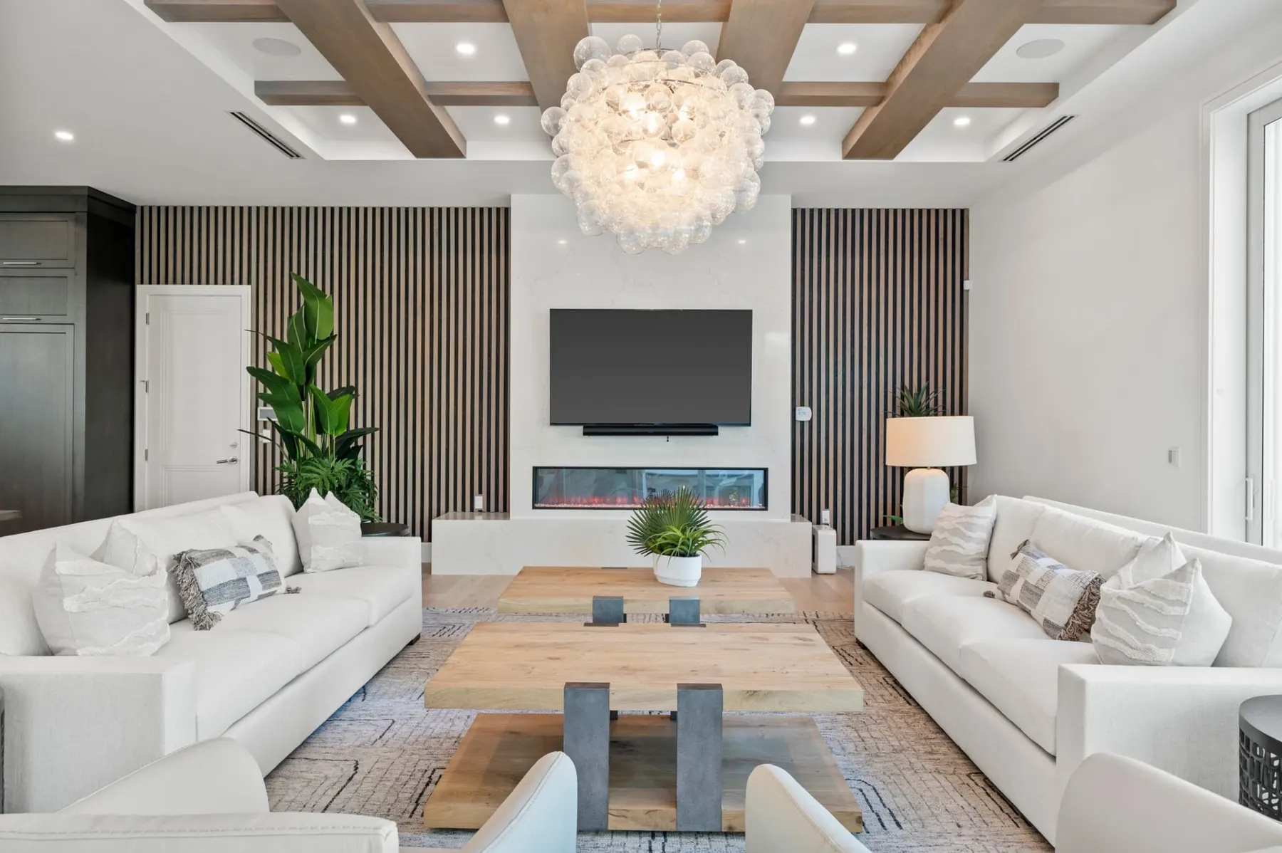 Living room seating group with white sofas, a slatted feature wall and a television above a linear fireplace.