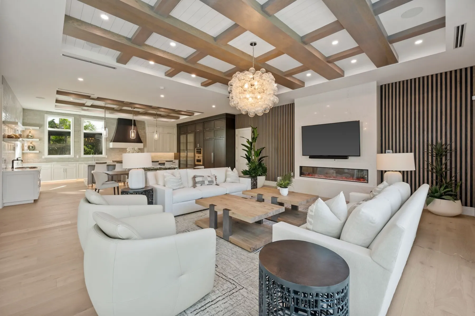 Living area looking toward the kitchen, with white sofas, a coffee table and a coffered ceiling with wood beams.