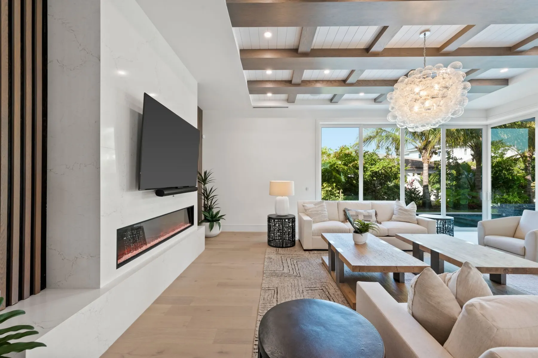 Fireplace wall with a wall-mounted television, a sectional sofa and large windows opening to the pool.