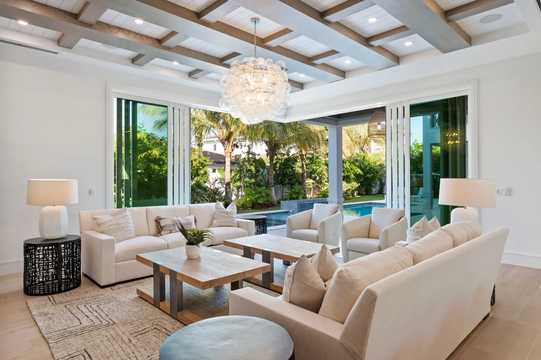 Living room with sliding glass doors open to the lanai and pool, under a coffered ceiling with wood beams.
