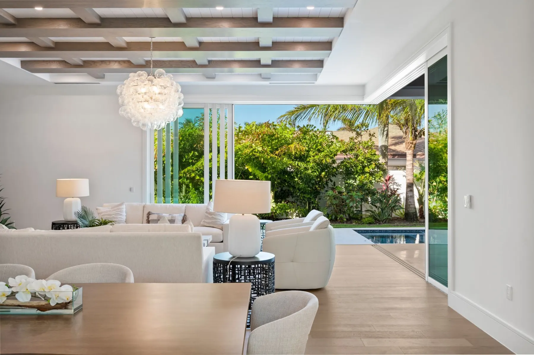 Dining table beside open sliding doors to the lanai and pool, under a bubble chandelier.