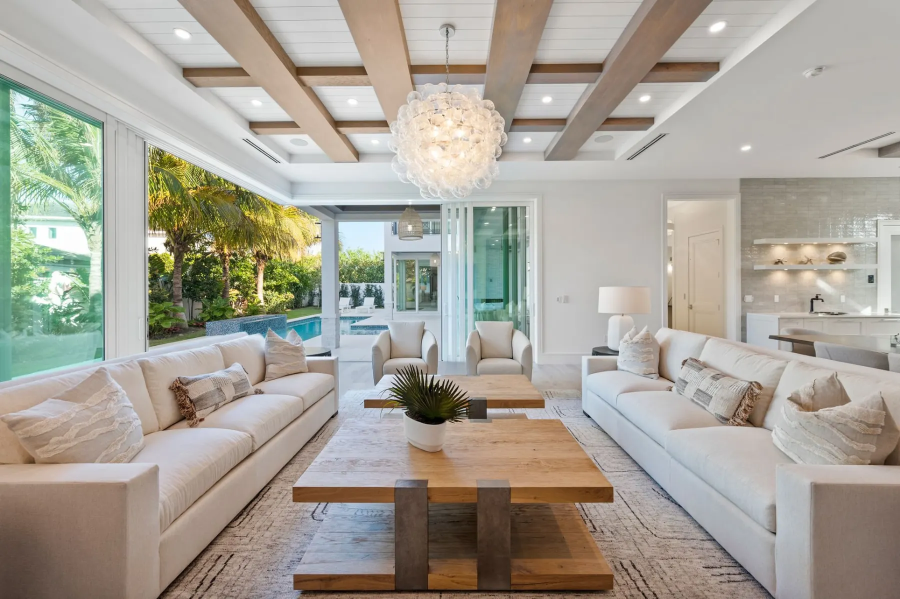 Living room sofas and a wood coffee table, with a bubble chandelier and glass doors to the pool beyond.