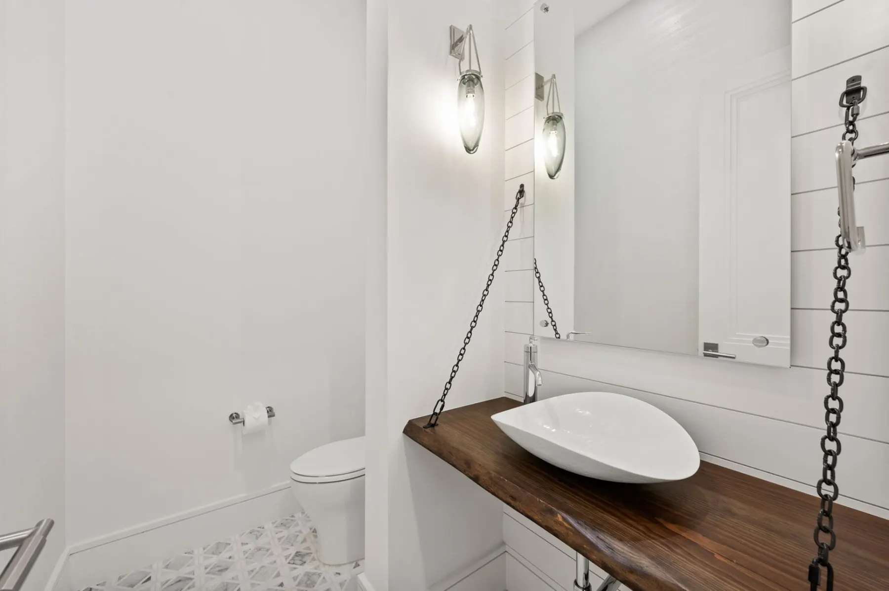 Powder room with a wall-hung wood vanity, a white vessel sink hung on chains and patterned floor tile.