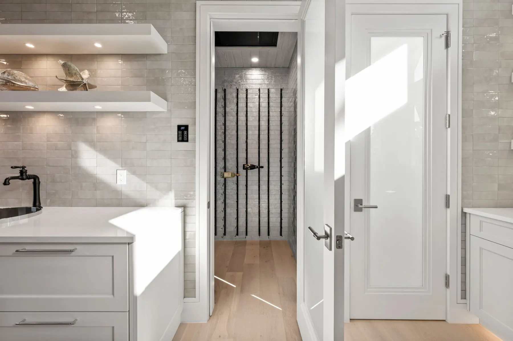 Wet bar corner with floating shelves, glazed tile and an open doorway to an adjoining room.