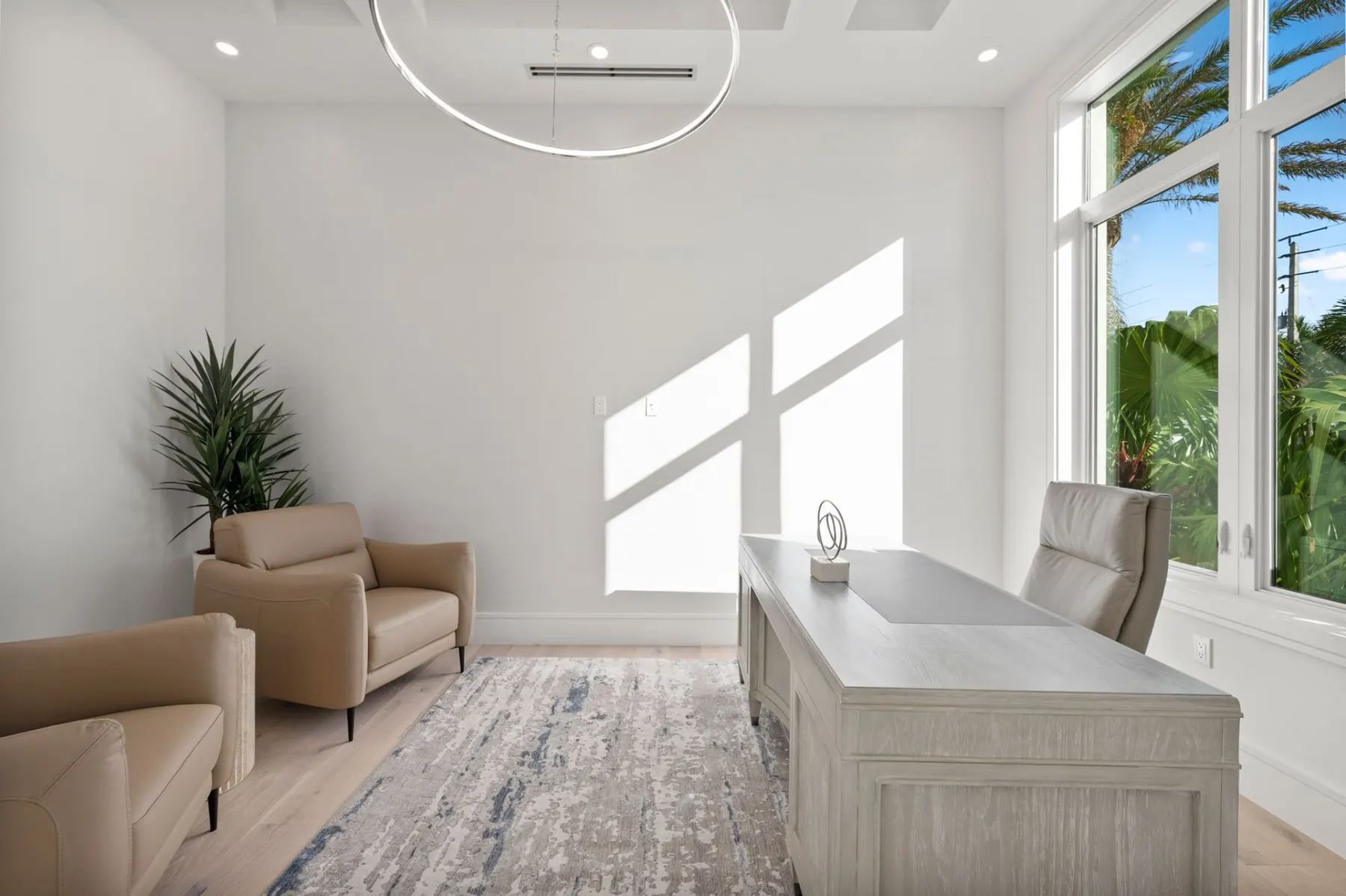 Home office with two leather armchairs, a desk, a ring chandelier and tall windows.