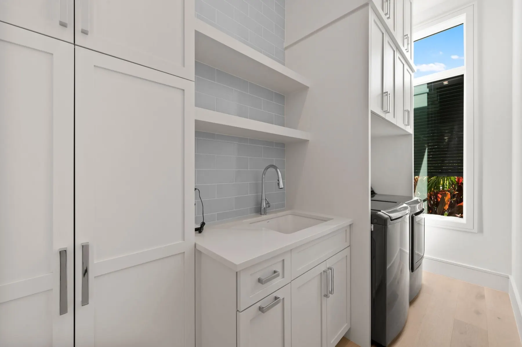 Room with white built-in cabinets, open shelves and a sink beside a window.