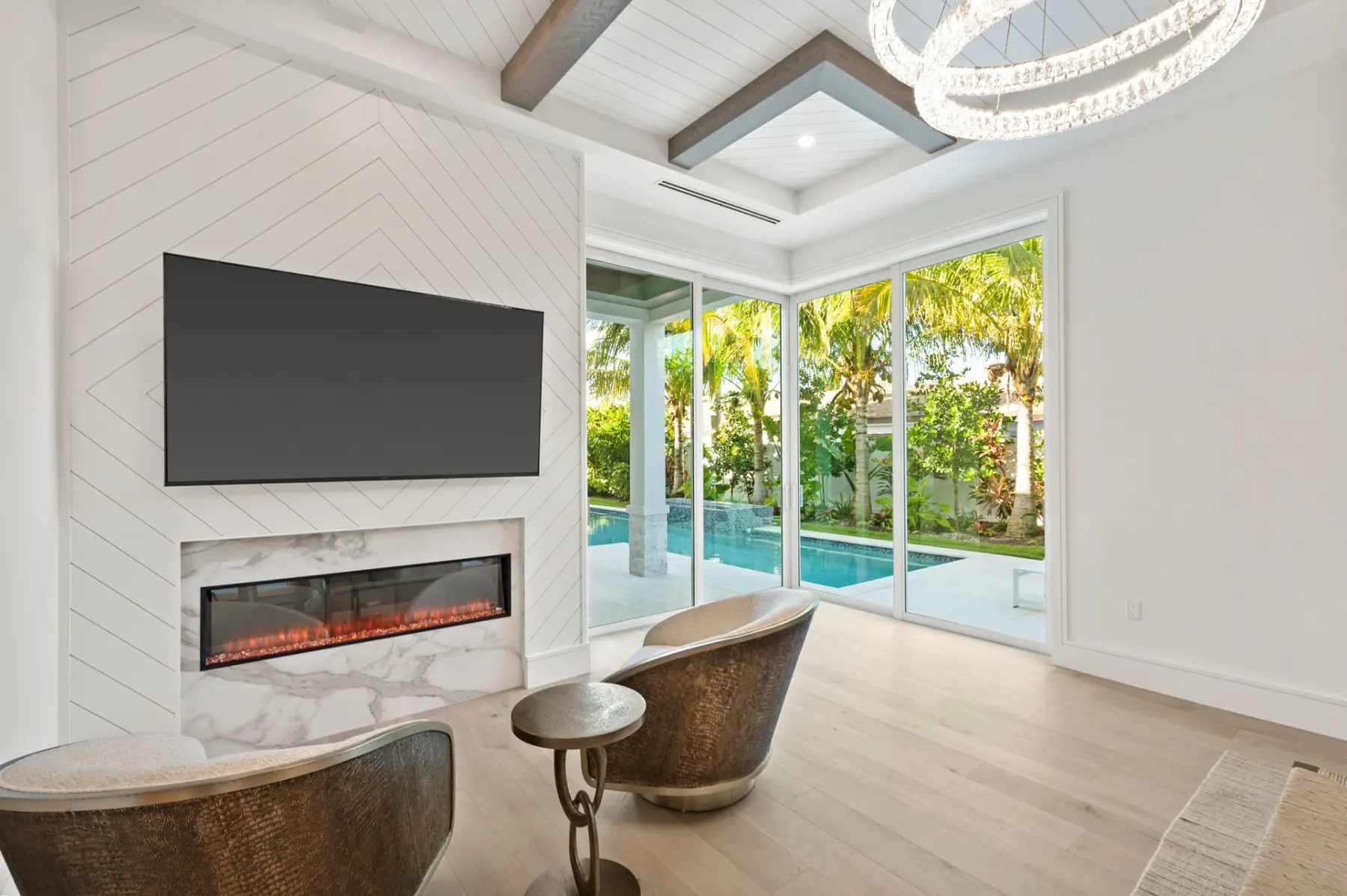 Primary bedroom with a chevron-pattern feature wall, a television, a linear fireplace and a beamed tray ceiling.