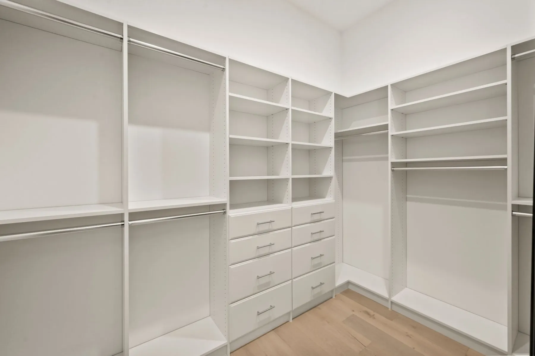 Primary walk-in closet with white built-in shelving, drawers and hanging rods.