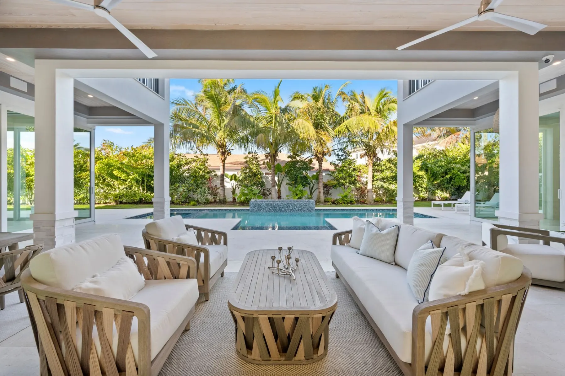 Covered lanai seating area with wicker sofas and a coffee table, looking out to the pool and palms.