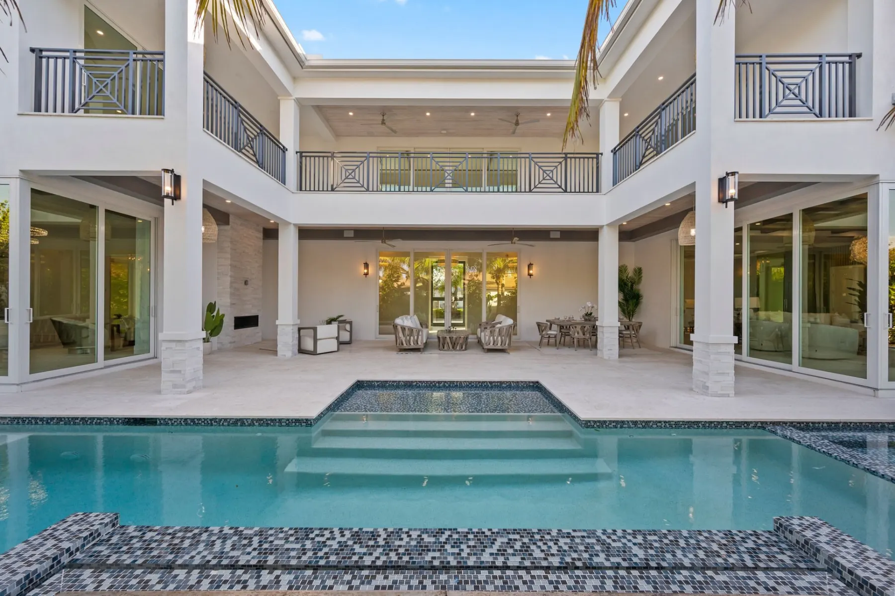 Rear of the home with a two-story covered terrace, balcony railings and the pool in front.