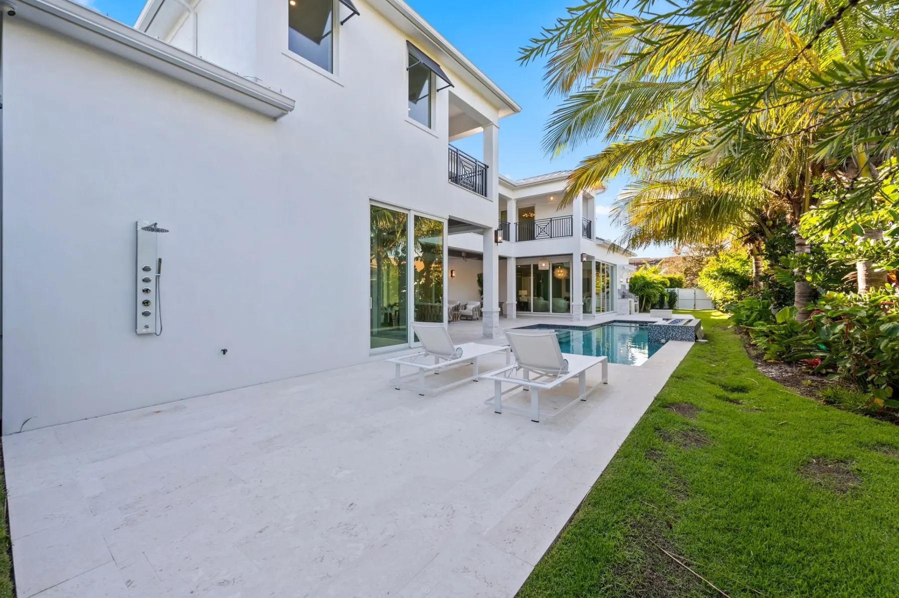 Stone paver terrace along the rear of the home with lounge chairs, an outdoor shower and the pool beyond.