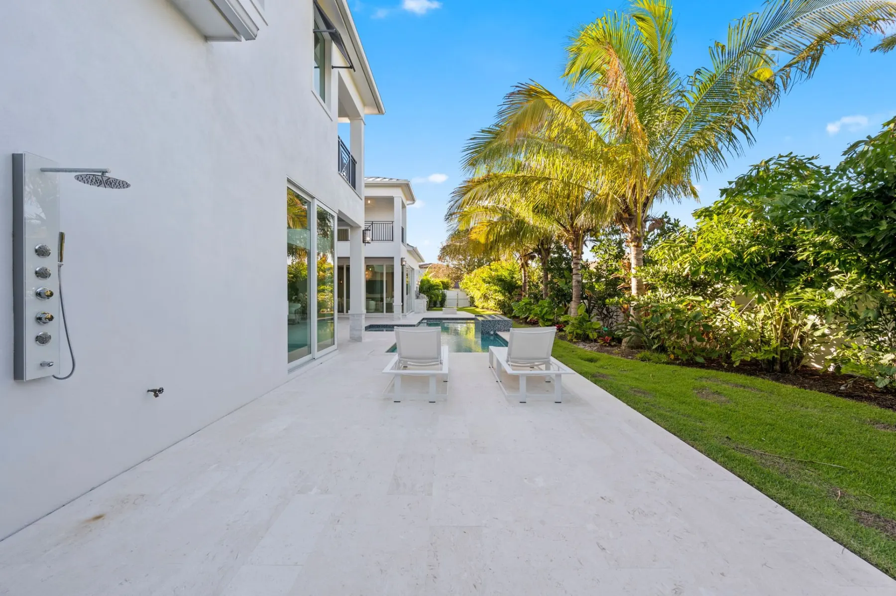 Pool terrace with an outdoor shower on the rear wall, lounge chairs and palms.