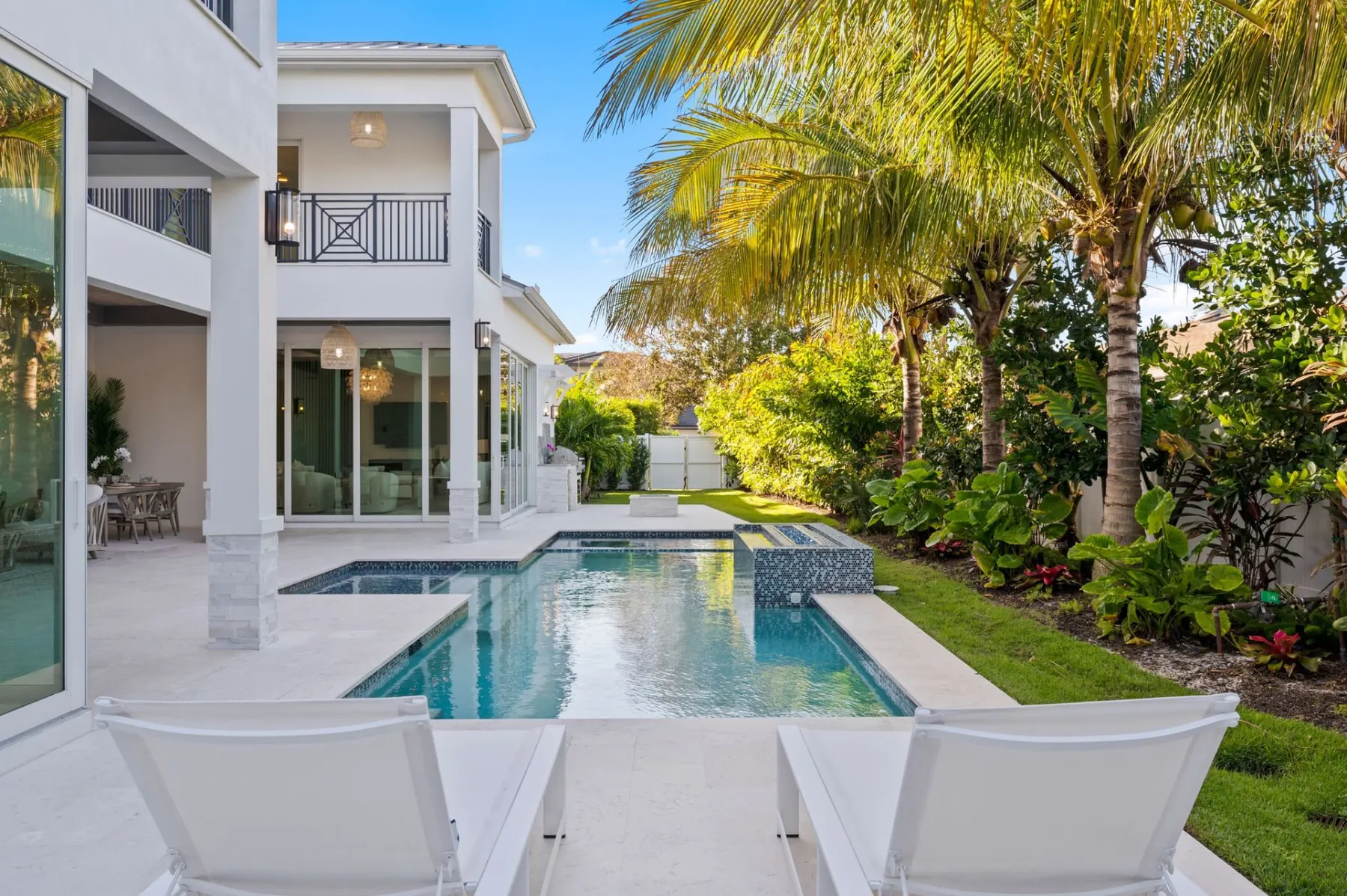 Pool and terrace with white lounge chairs, with the covered terraces and balconies of the home behind.