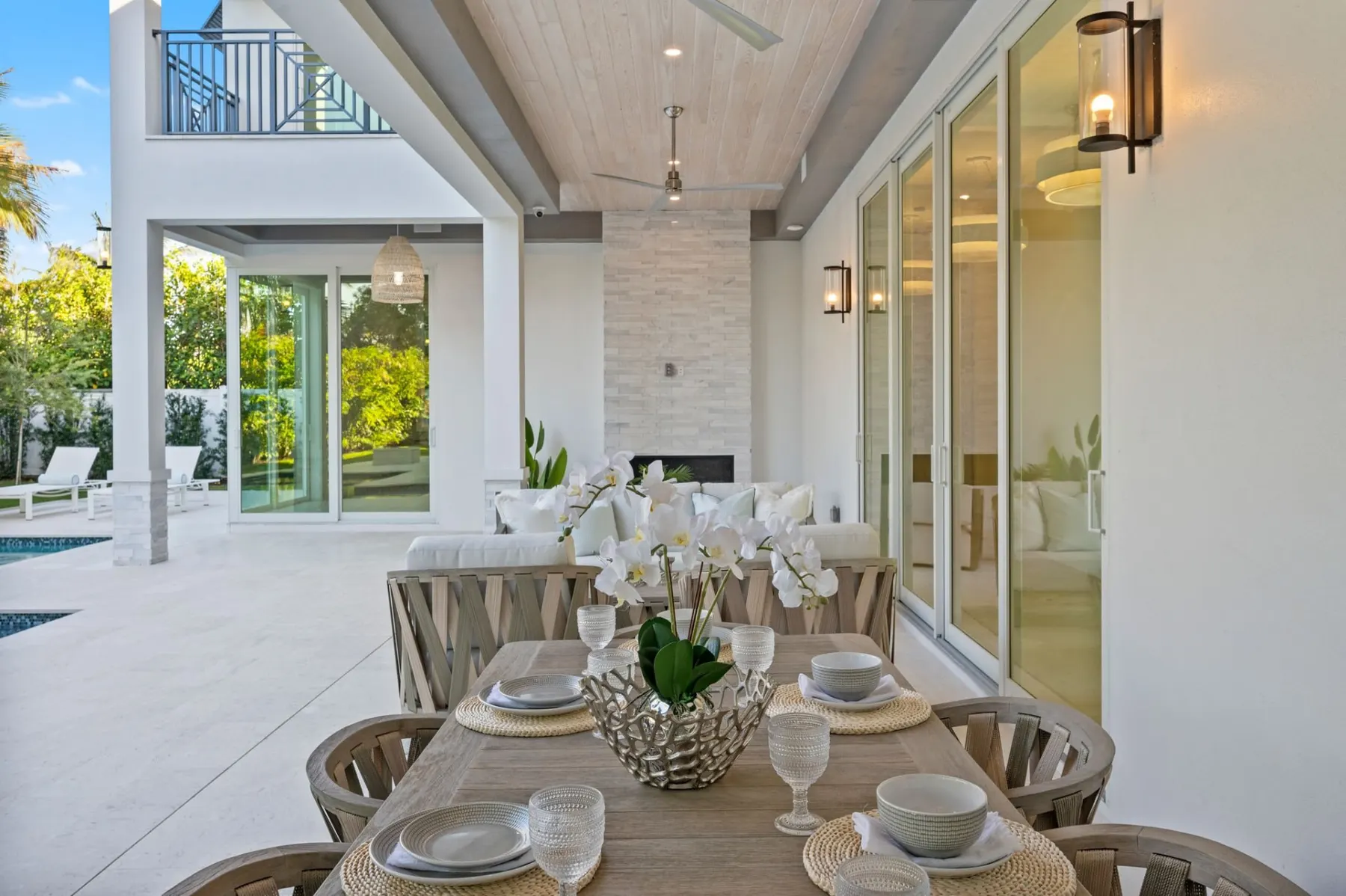 Covered lanai dining table with a stacked-stone fireplace column and sliding glass doors.