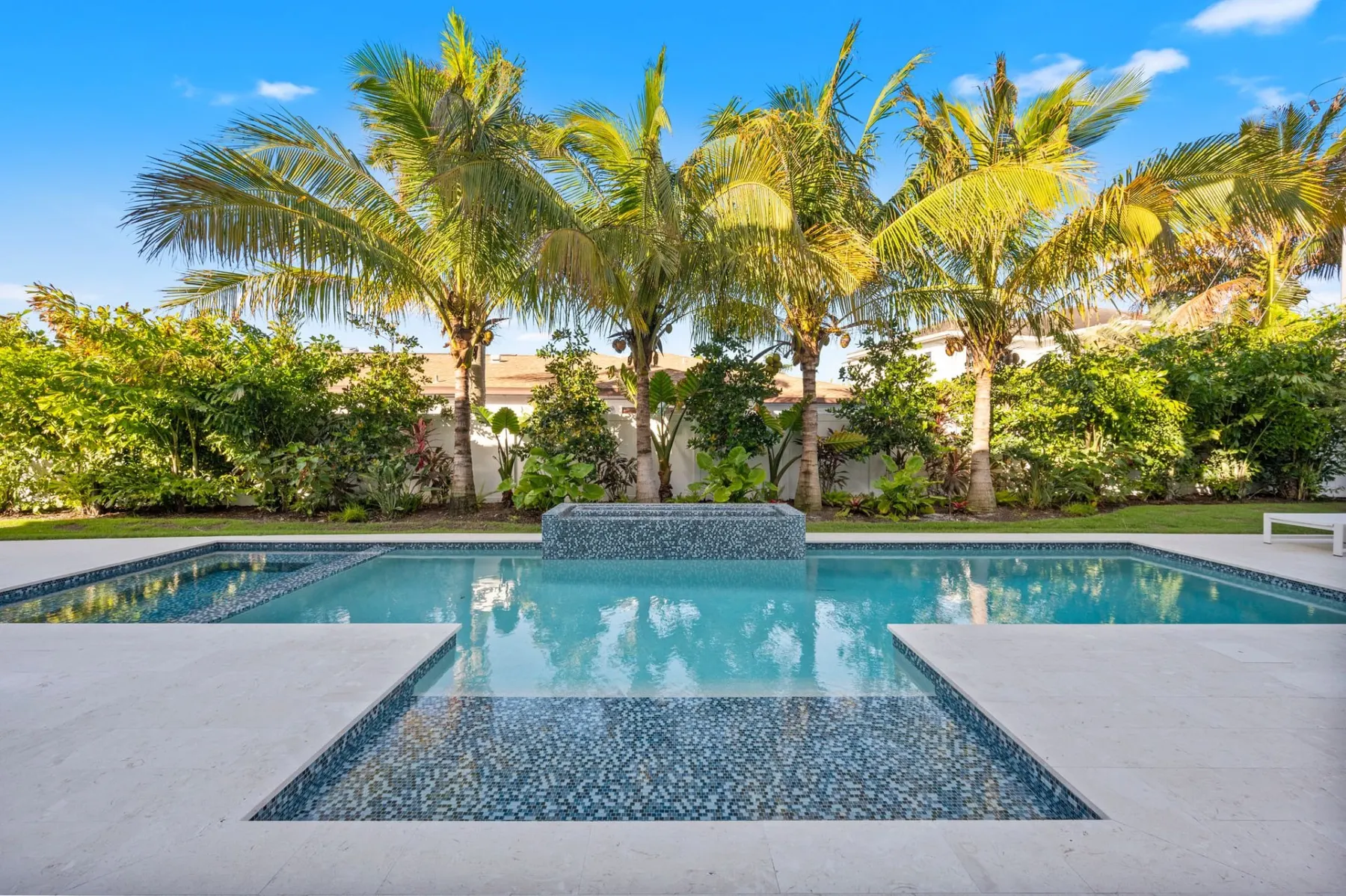 Pool with a raised spa and tile sun shelf framed by palms and landscaping.