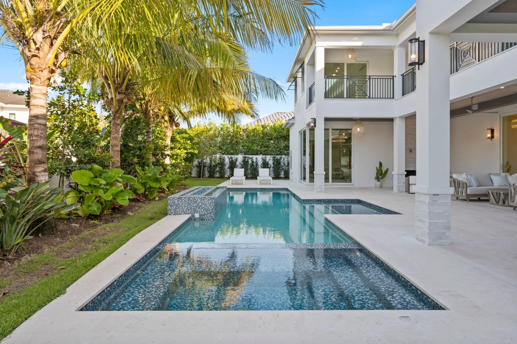 Pool with a raised spa and blue mosaic tile steps, with palms and landscaping around it.