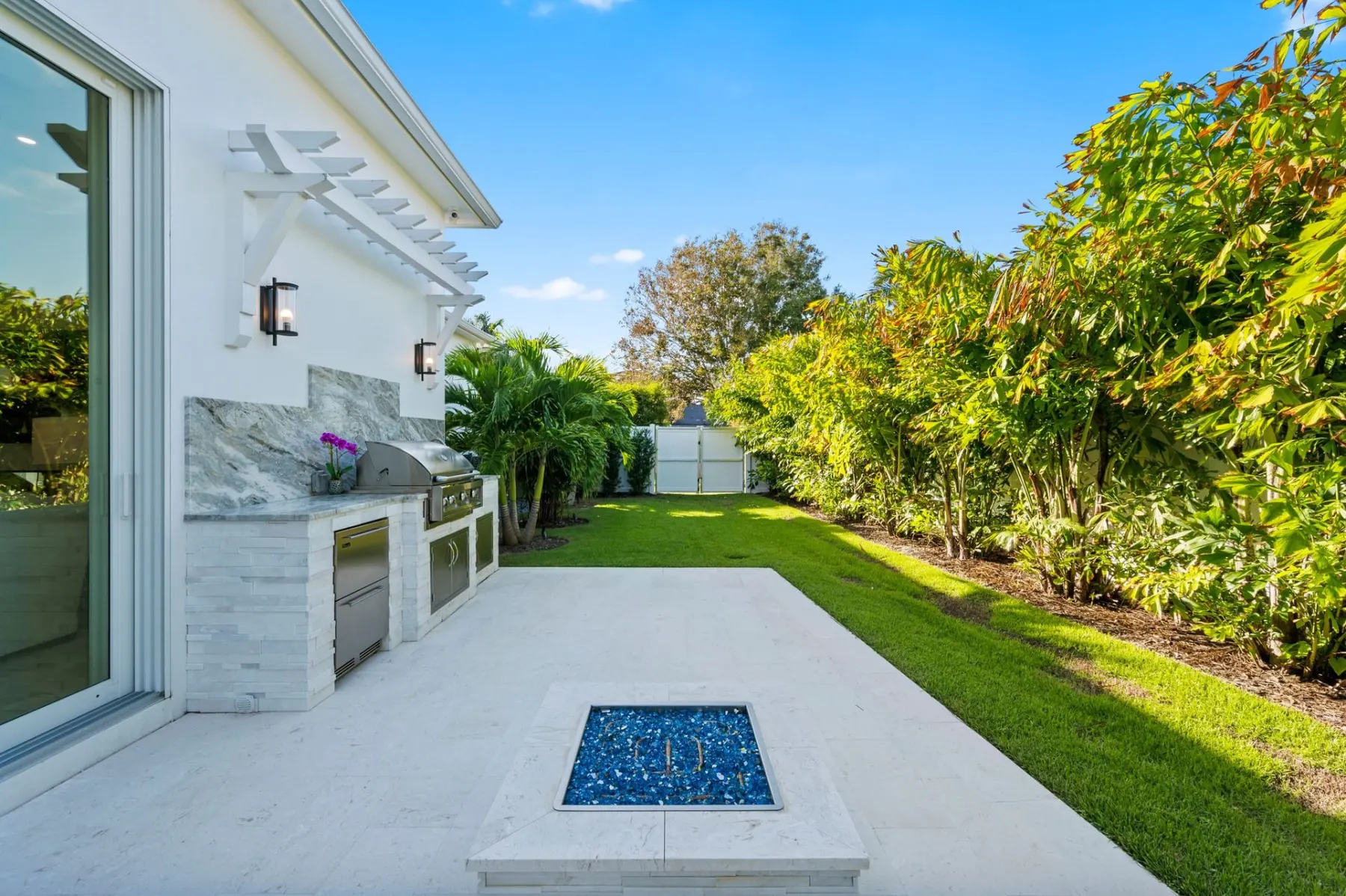 Backyard lawn and outdoor kitchen with a fire pit, beside the sliding glass walls of the great room.
