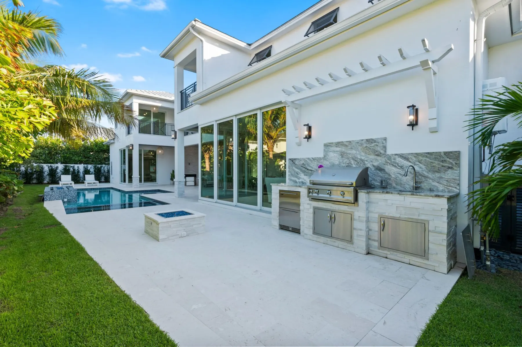 Outdoor kitchen with a built-in grill, a fire pit and sliding glass doors beside the pool.