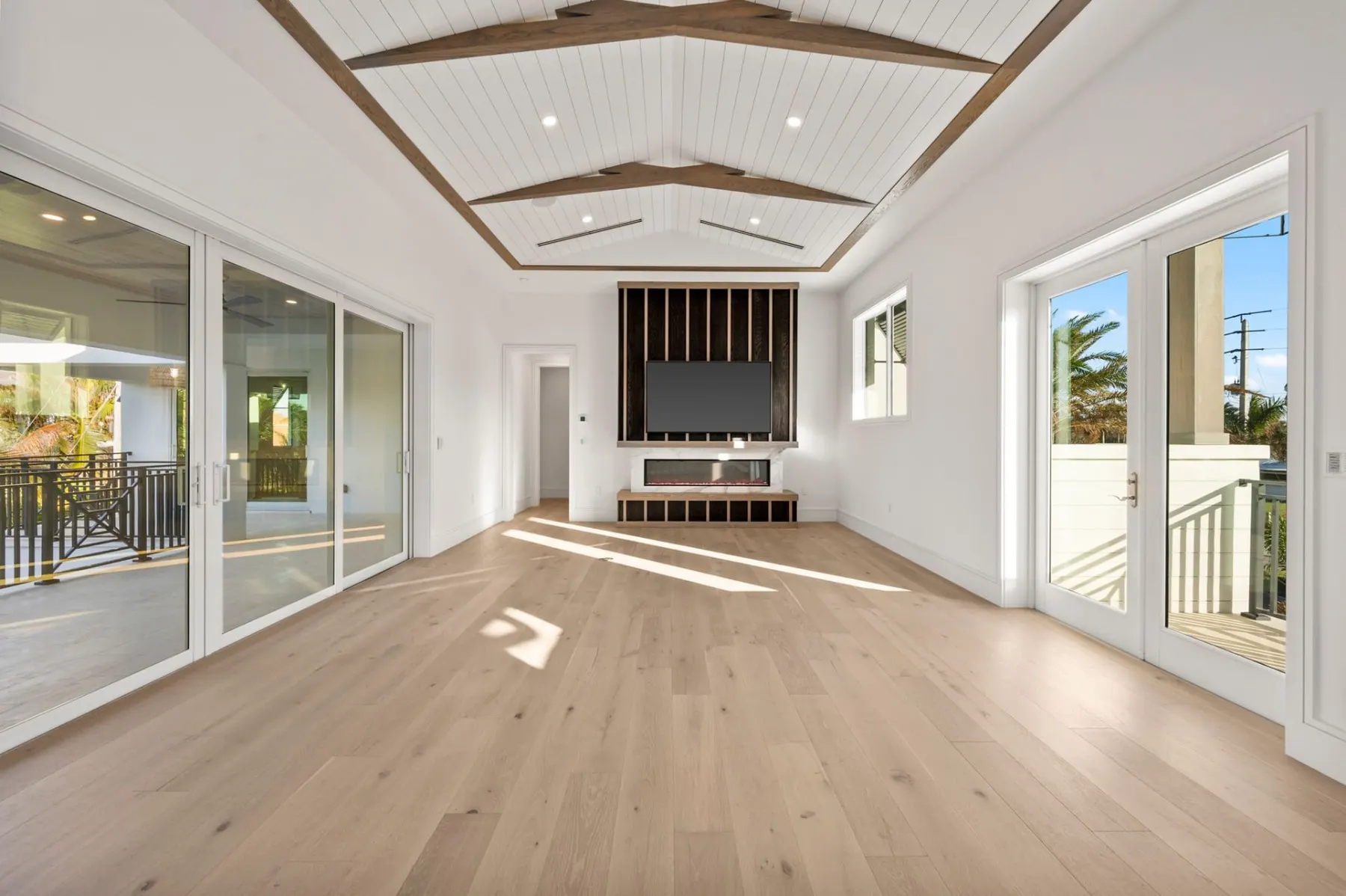 Upstairs lounge with a media wall, wood floors and sliding glass doors to a balcony.