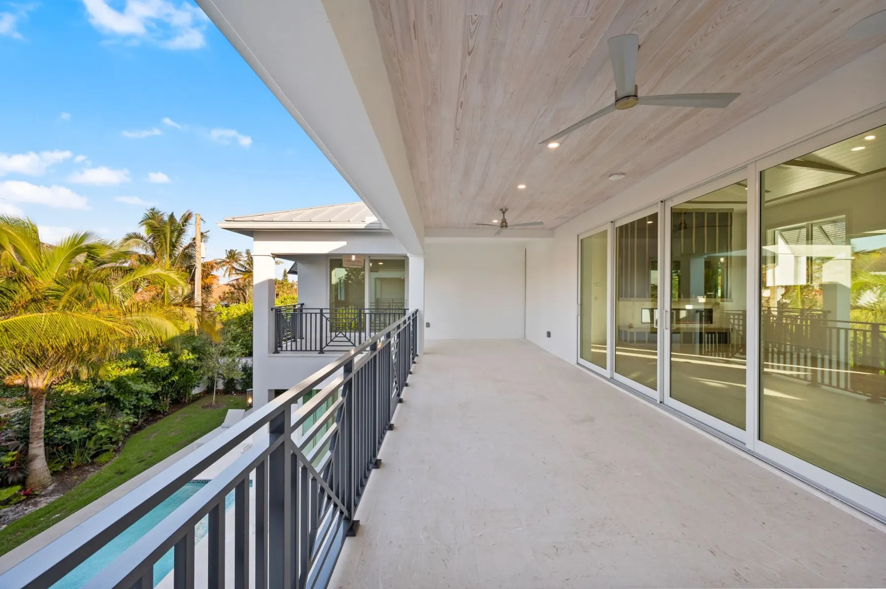 Upstairs balcony with a dark railing, a plank ceiling and sliding glass doors.