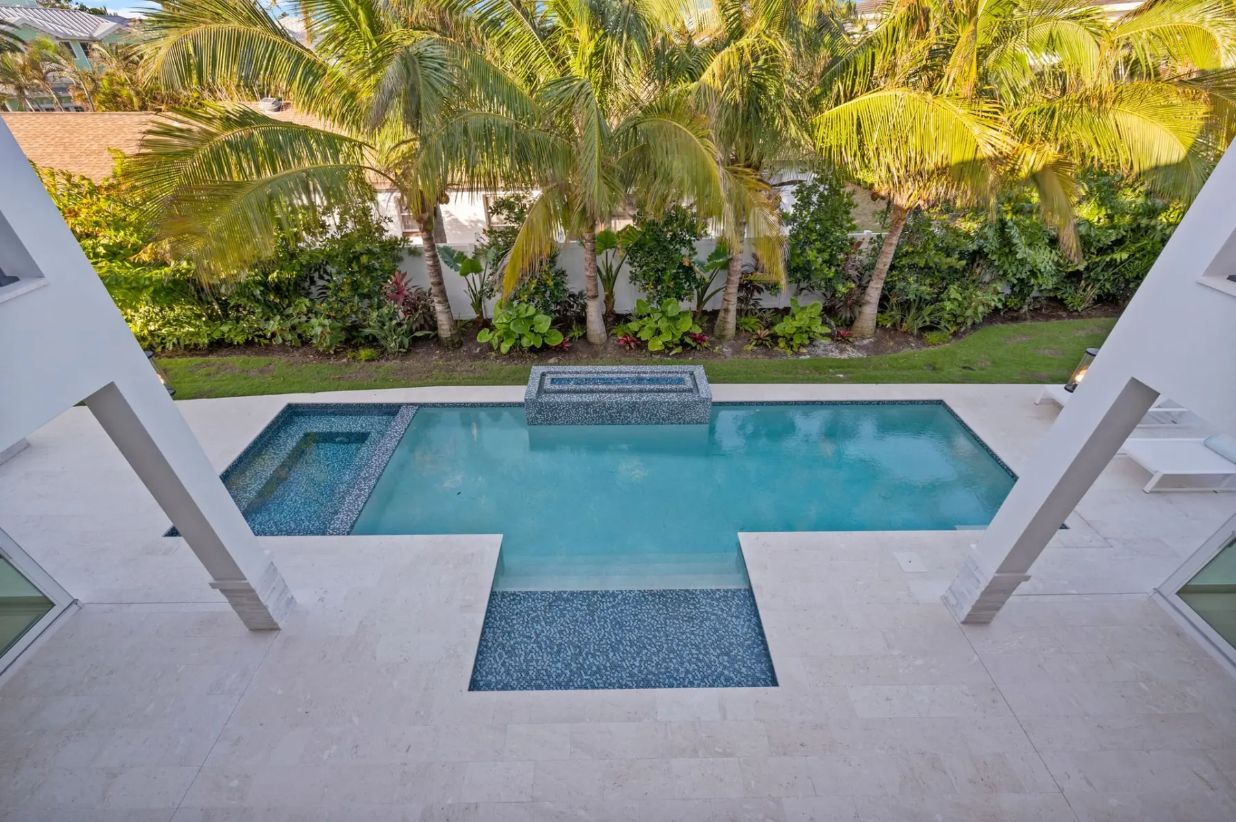 View down to the pool and spa between terrace columns, with palms behind.