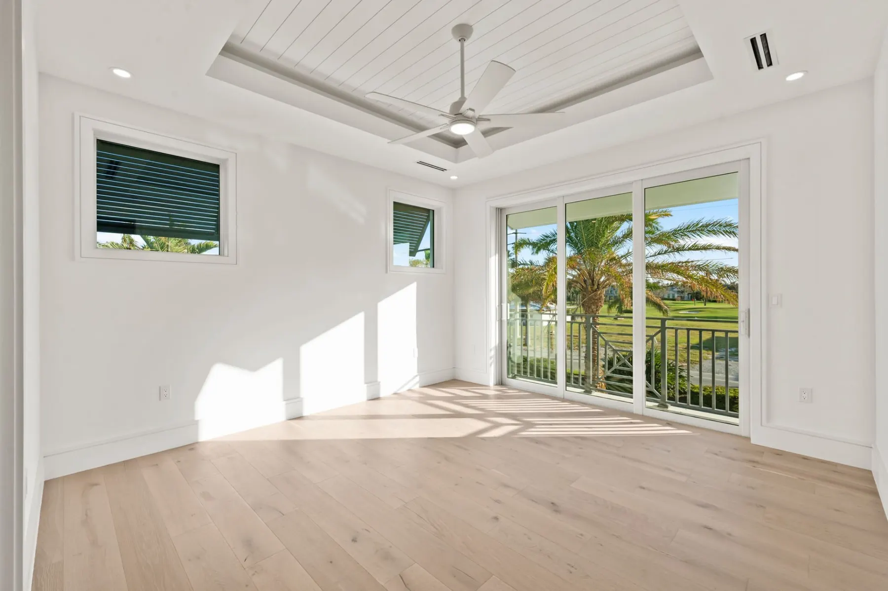 Upstairs bedroom with a tray ceiling and fan, a window and a sliding door to the balcony.
