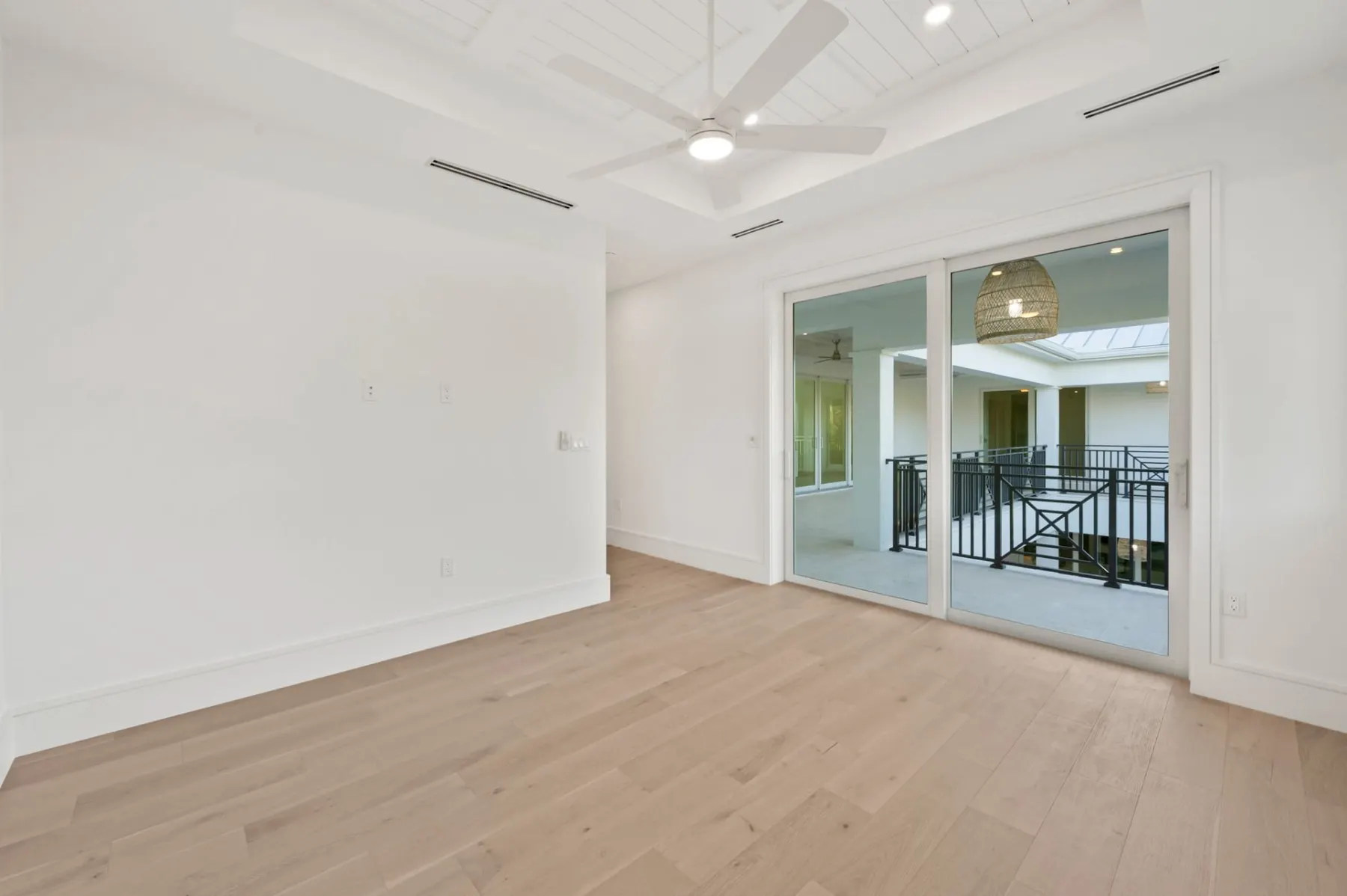 Upstairs bedroom with a sliding door to a balcony and a tray ceiling with a fan.