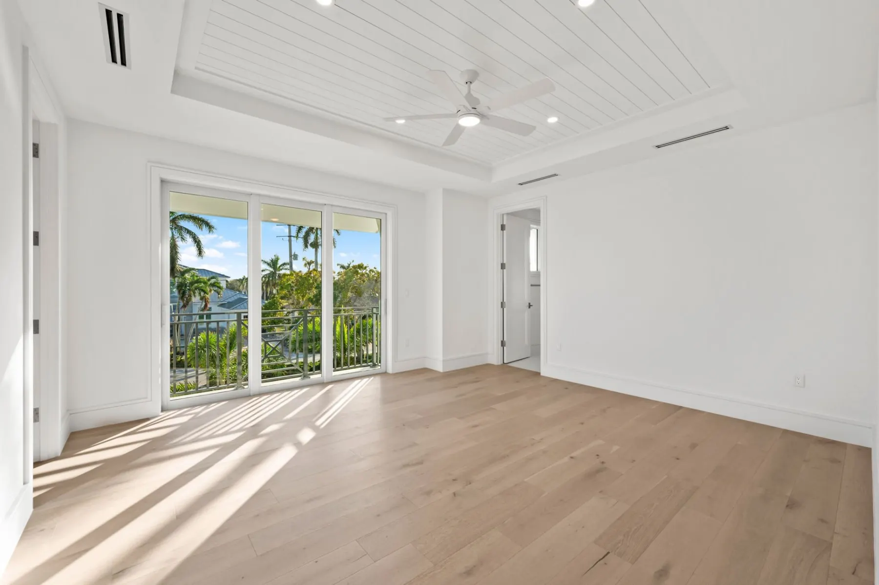 Upstairs bedroom with a planked tray ceiling, a ceiling fan and sliding glass doors.