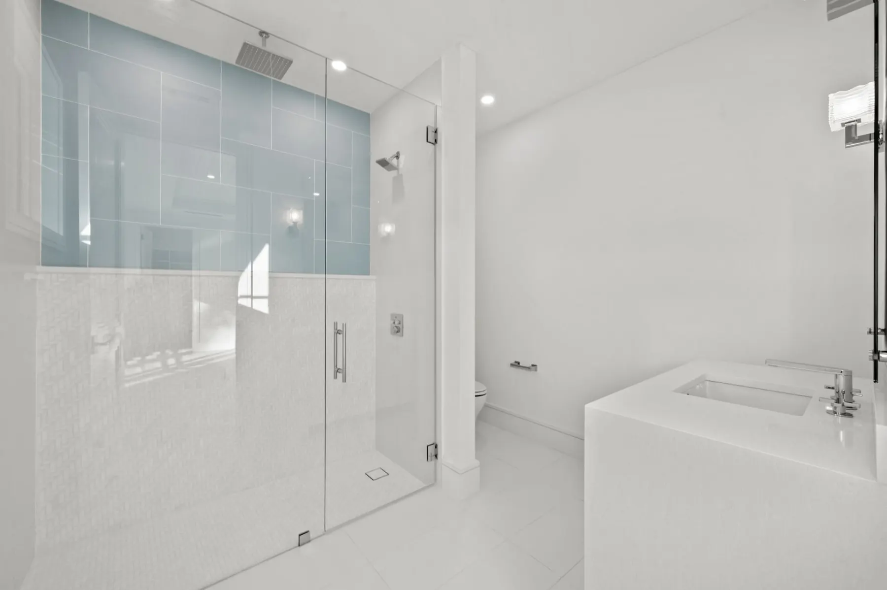 Bath with a glass-enclosed shower, a blue glass tile band and a white vanity.