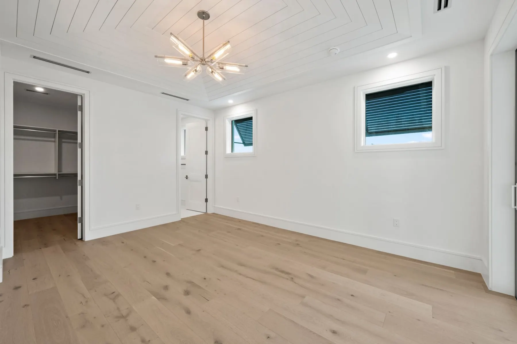 Upstairs bedroom with a sunburst chandelier, a walk-in closet entry and wood floors.