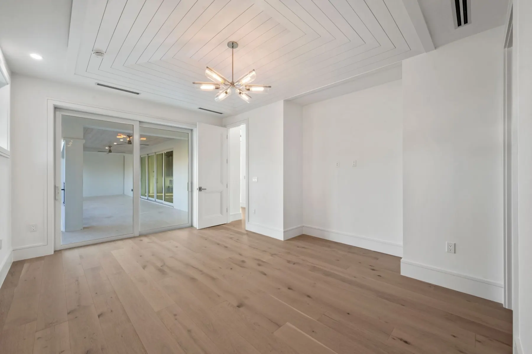 Upstairs bedroom with a sunburst chandelier and glass doors.