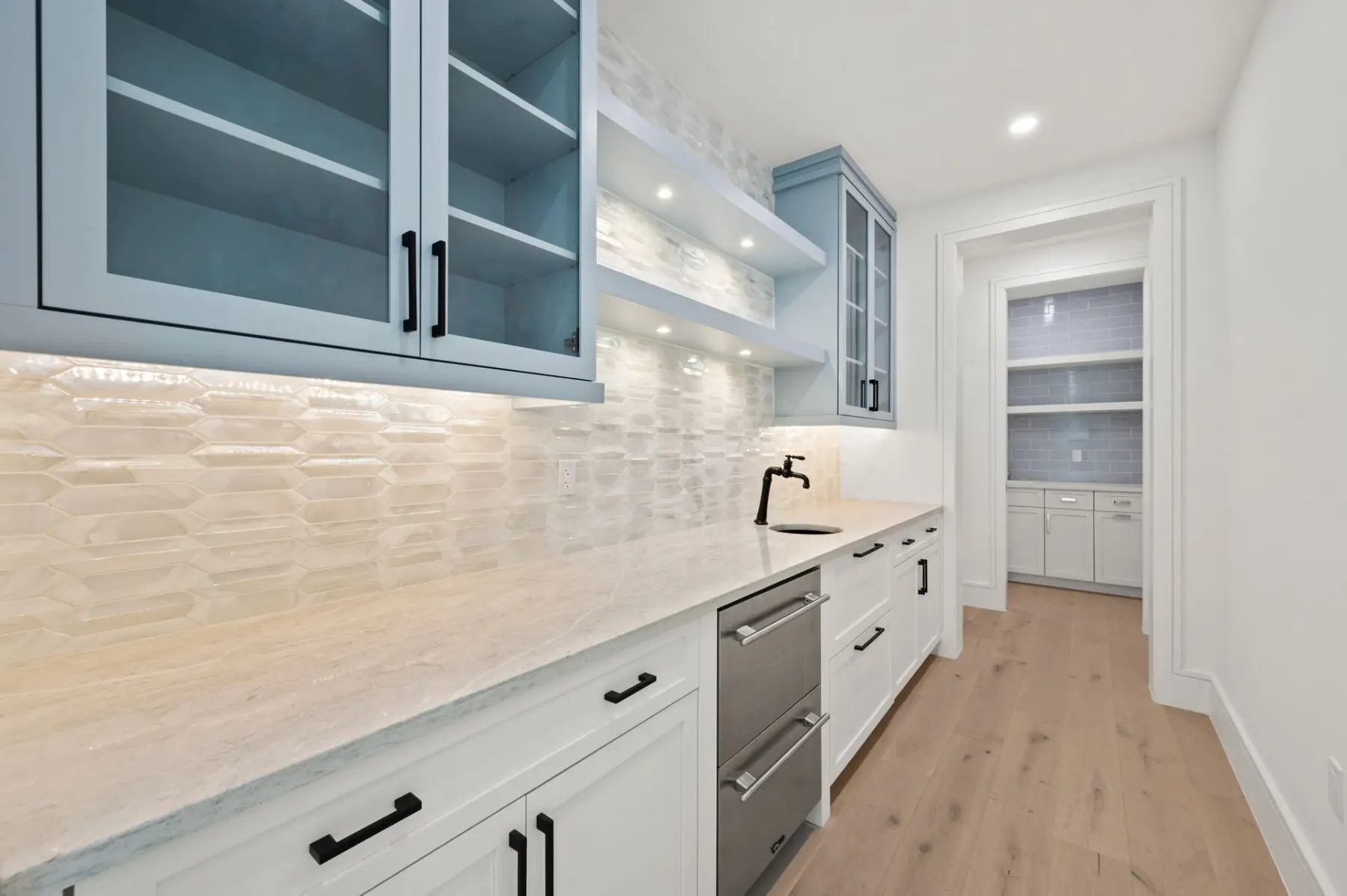 Pantry area with light blue glass-front cabinets, a white counter and a tile backsplash.