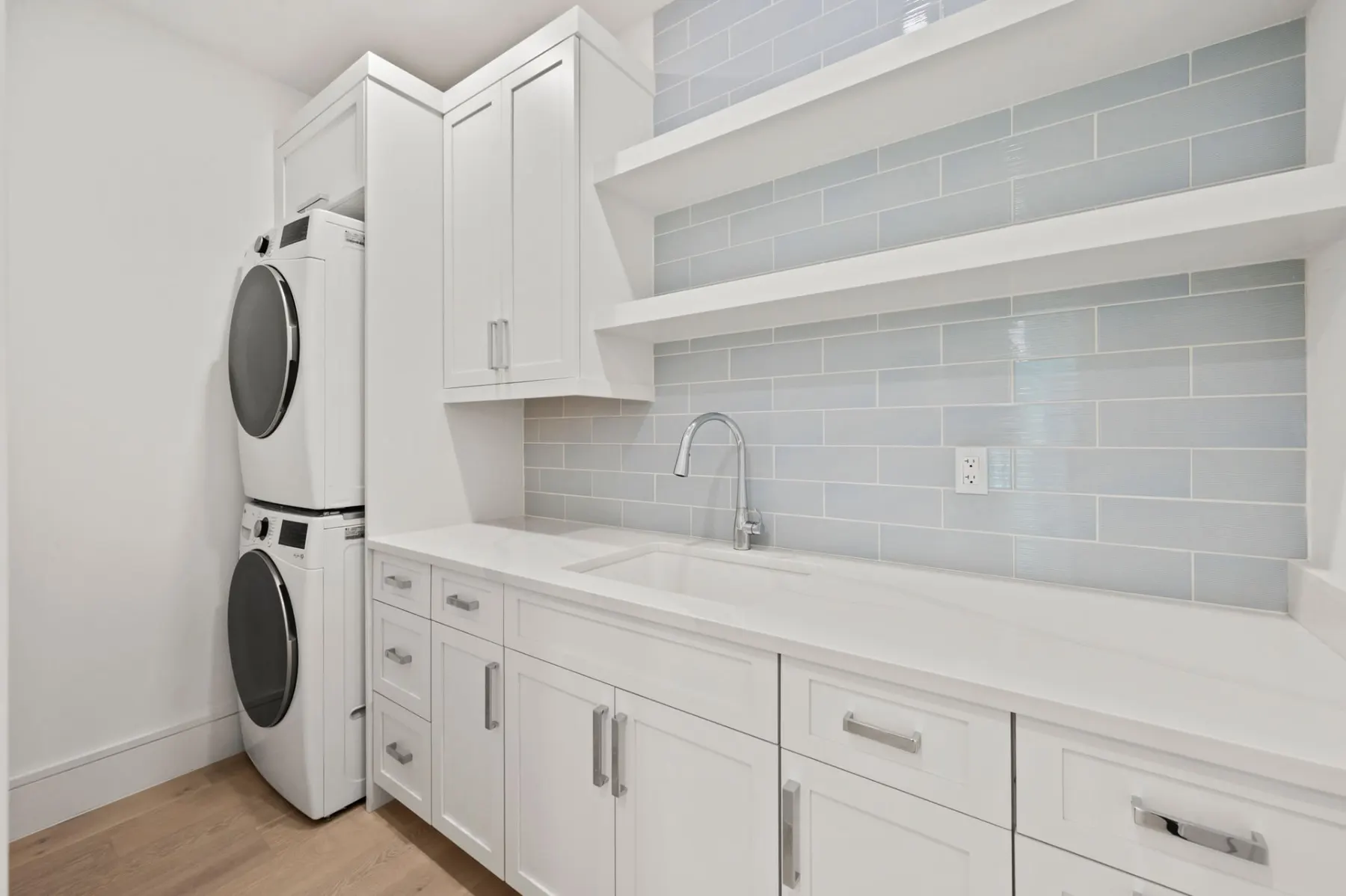 Laundry room with a stacked washer and dryer, white cabinets, a sink and a glass tile backsplash.