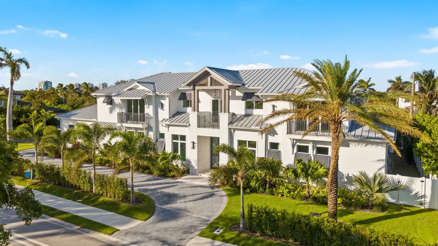 Aerial view of the front of the home with a gray standing-seam metal roof, a gabled entry and a curved paver motor court.