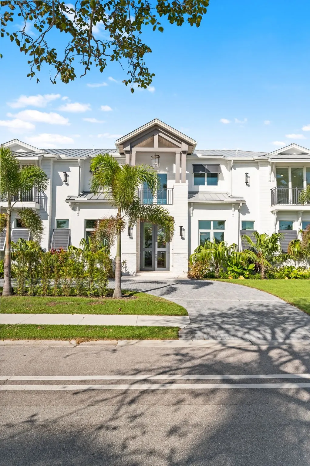 Portrait view of the front of the home with a gabled entry, balcony railings and palms framing the two-story facade.
