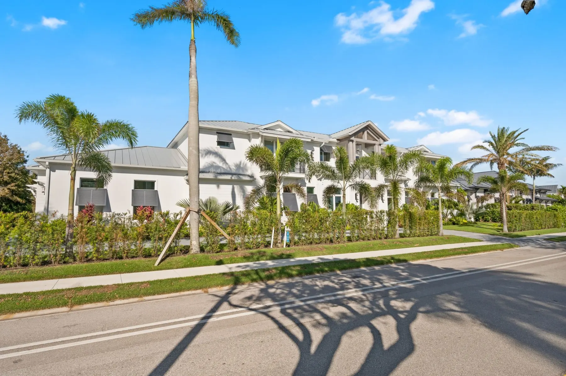Side of the home from the street, with a metal roof, bahama shutters and a long hedge along the sidewalk.