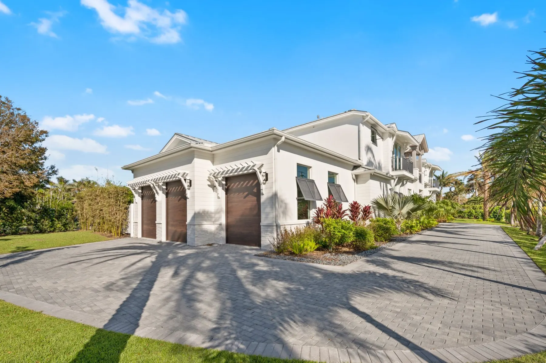 Side garage wing with three wood-look garage doors, white trellis brackets and a paver motor court.