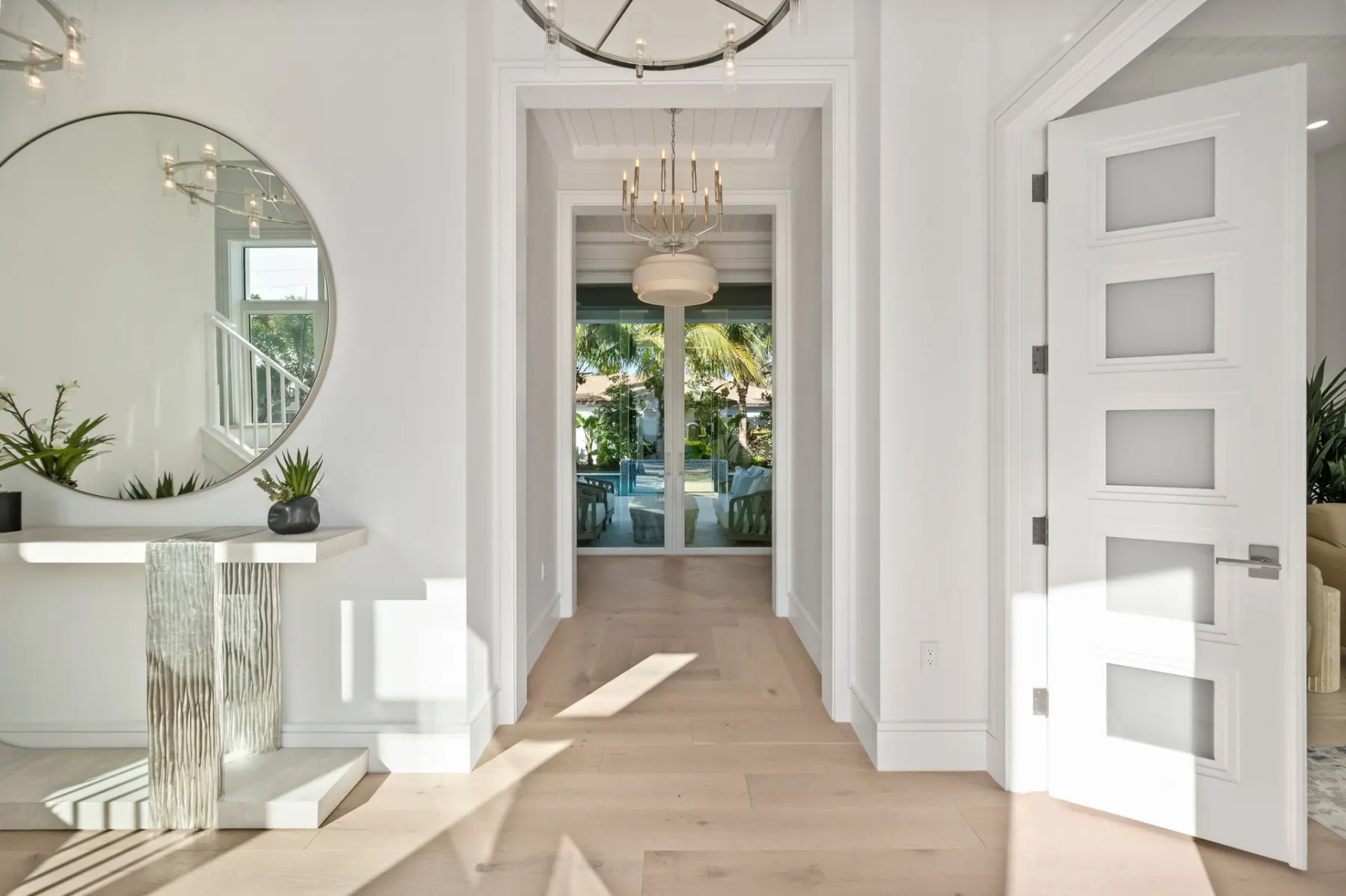 Foyer with a round mirror, a console table, a white paneled door and a view through glass doors to the lanai and pool.